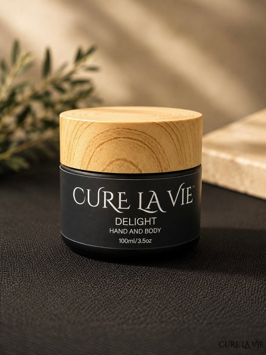 Cure La Vie DELIGHT Hand and Body Crème 100ml jar with wood lid on dark surface with soft botanical sprig