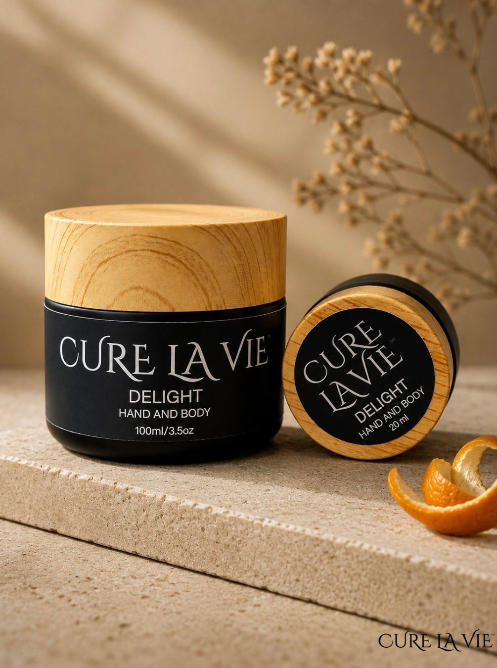 Cure La Vie DELIGHT Hand and Body Crème 100ml and 20ml jars displayed together with fresh orange peel on stone surface